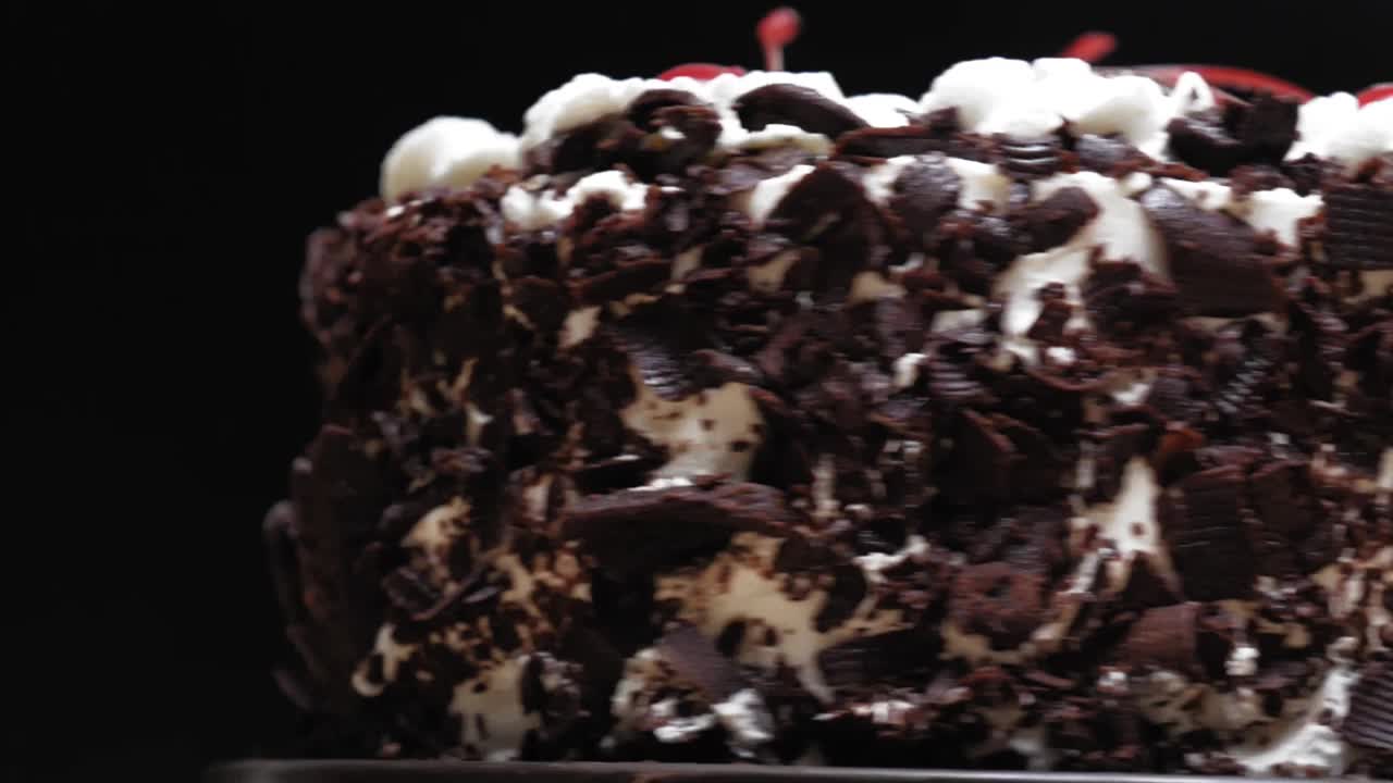旋转黑巧克力蛋糕在黑色背景，慢动作。视频下载