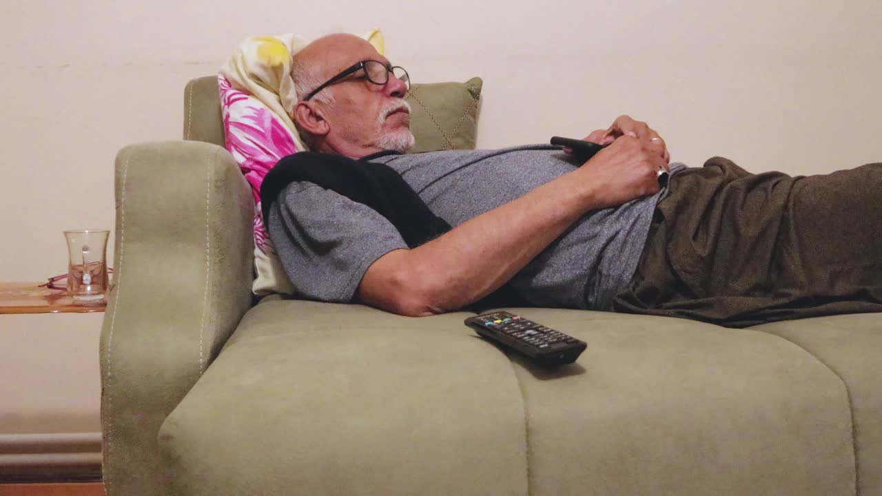 老人在看电视的时候，手拿手机，沙发遥控器睡着了视频素材