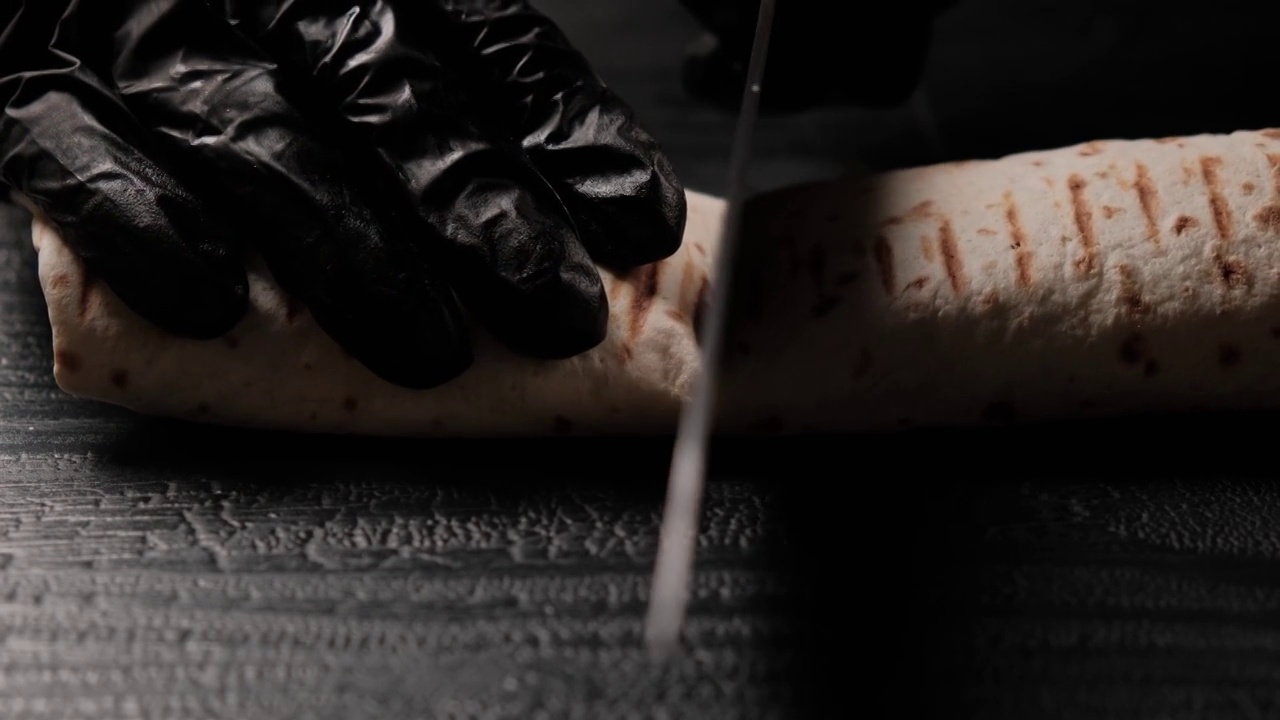 在一张黑色桌子的特写镜头中，沙瓦玛被一把刀切开视频素材