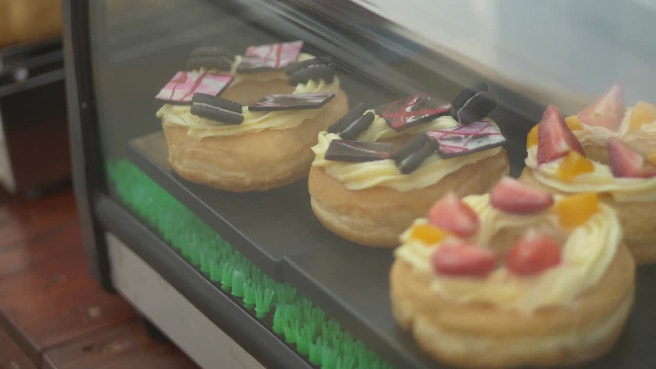 带配料的甜甜圈陈列在橱窗里出售。视频下载