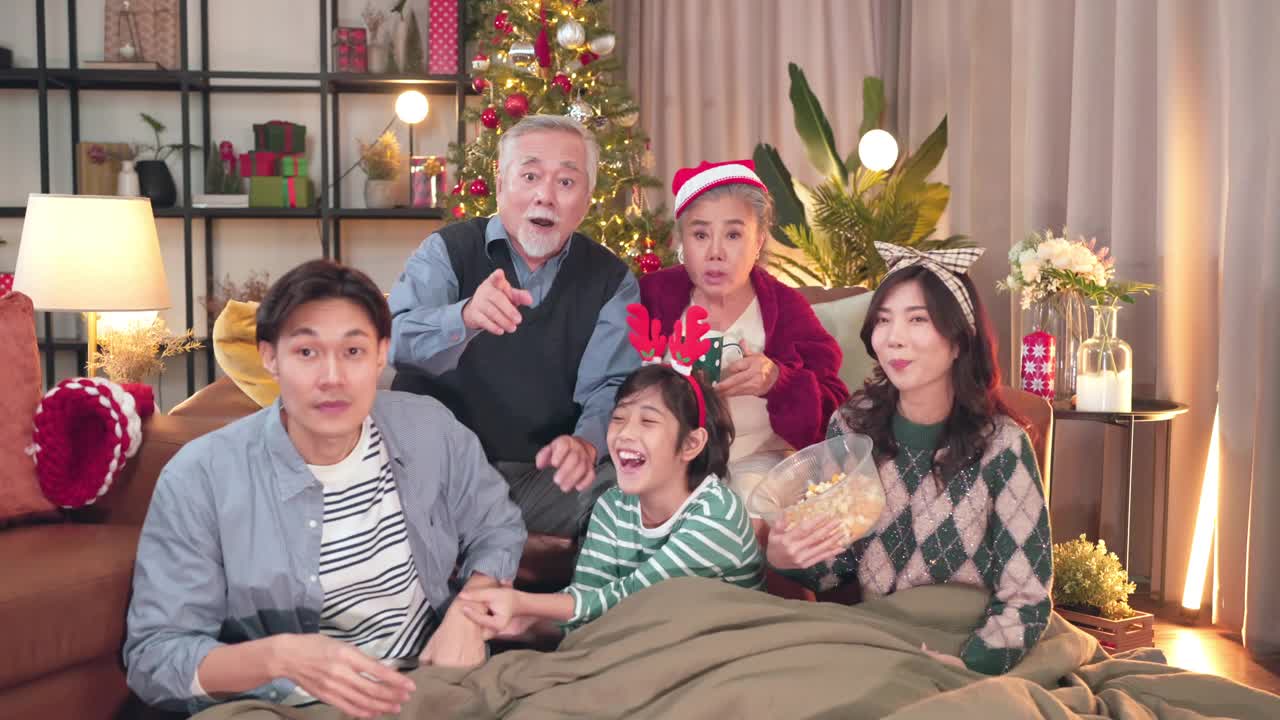 幸福亚洲家庭在家里一起度过欢乐的节日时刻，多代家庭祖父母、父母和孩子在圣诞节期间在家一起看喜剧电影视频下载
