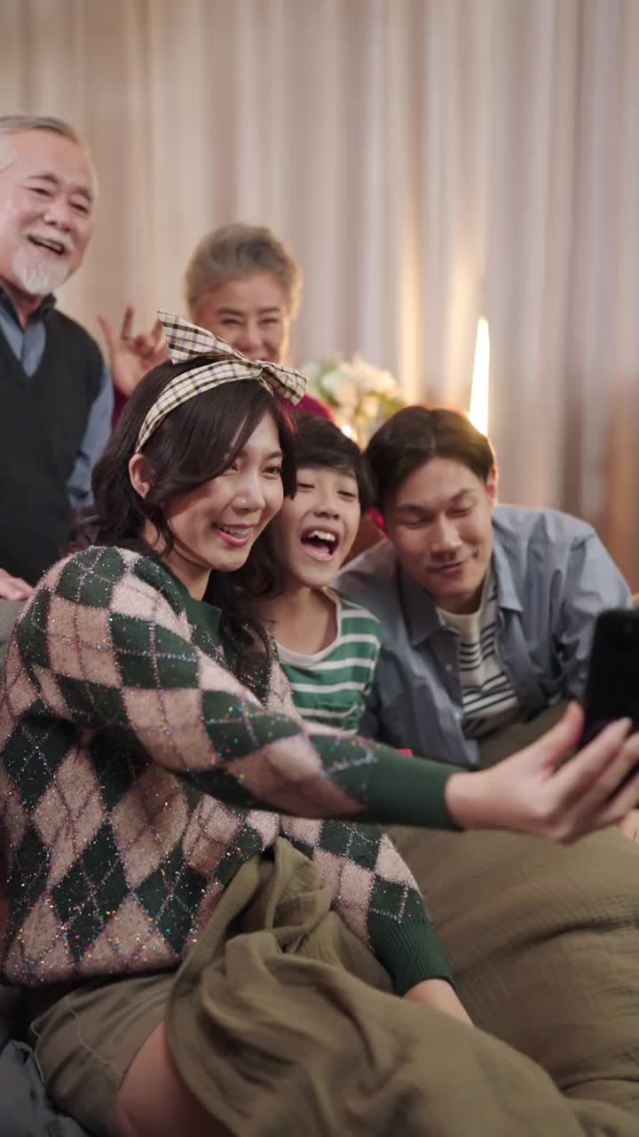 垂直拍摄多代亚洲家庭，幸福，世代和人的概念——幸福家庭坐在家里客厅的沙发上，一起用智能手机自拍视频素材