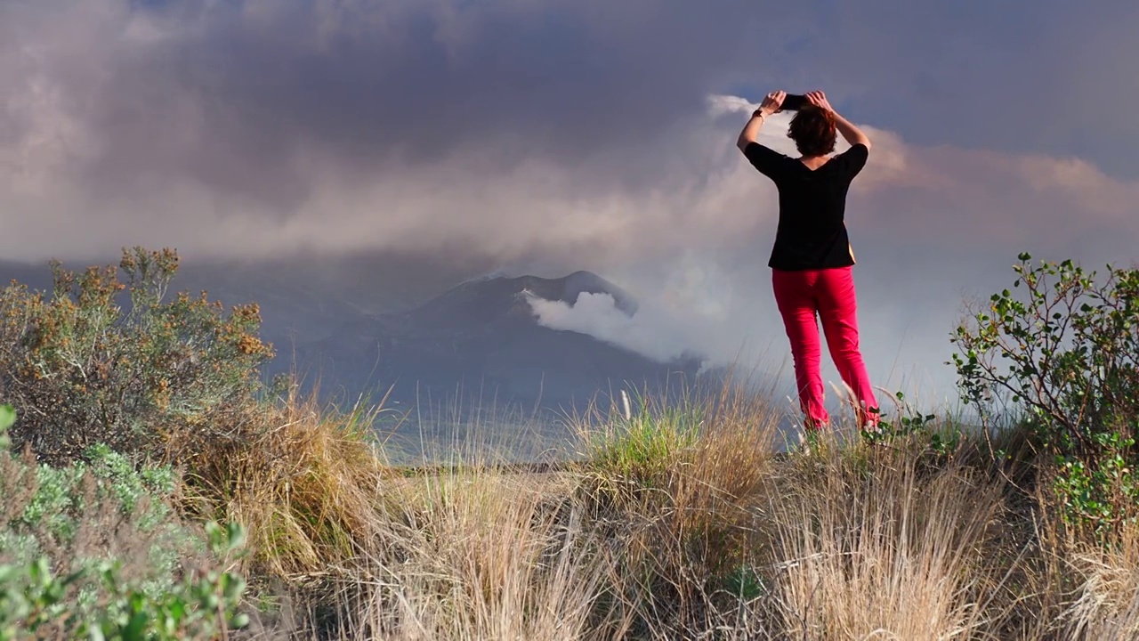 一名女子正在用手机拍摄喷发的火山。俯瞰康伯维哈火山，浓烟和熔岩柱从主锥中喷出。视频下载