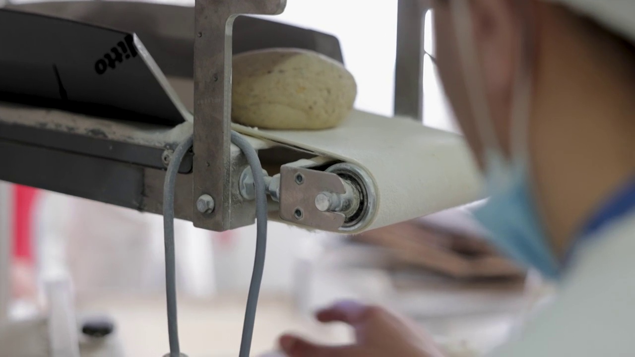面团滚压机，在生产线上弹出面团，同时烘烤师观察过程视频素材