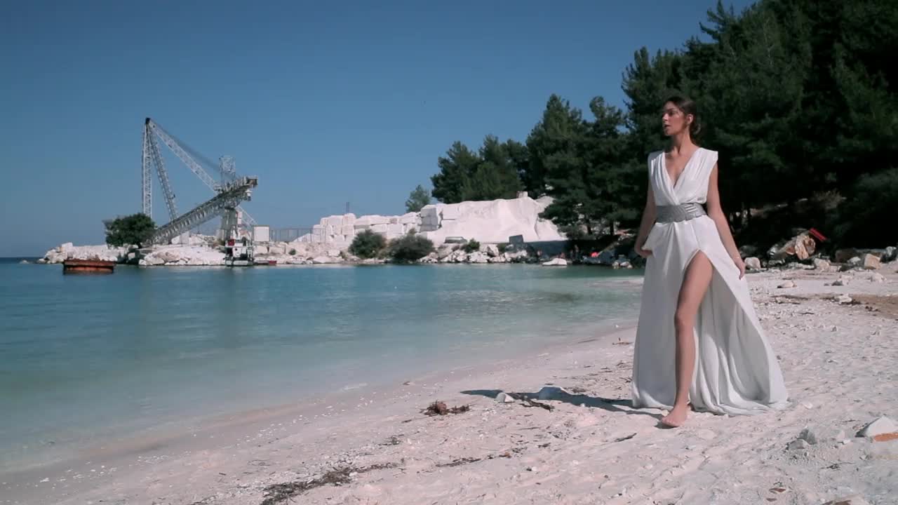 年轻漂亮的时装模特在沙滩上漫步，身穿设计师设计的白色连衣裙视频下载