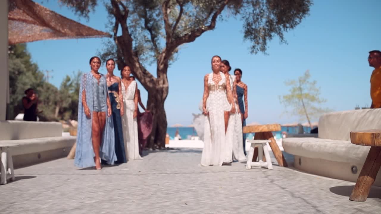 一群漂亮的年轻时装模特穿着设计师设计的飘逸的夏装在海滩上练习视频下载