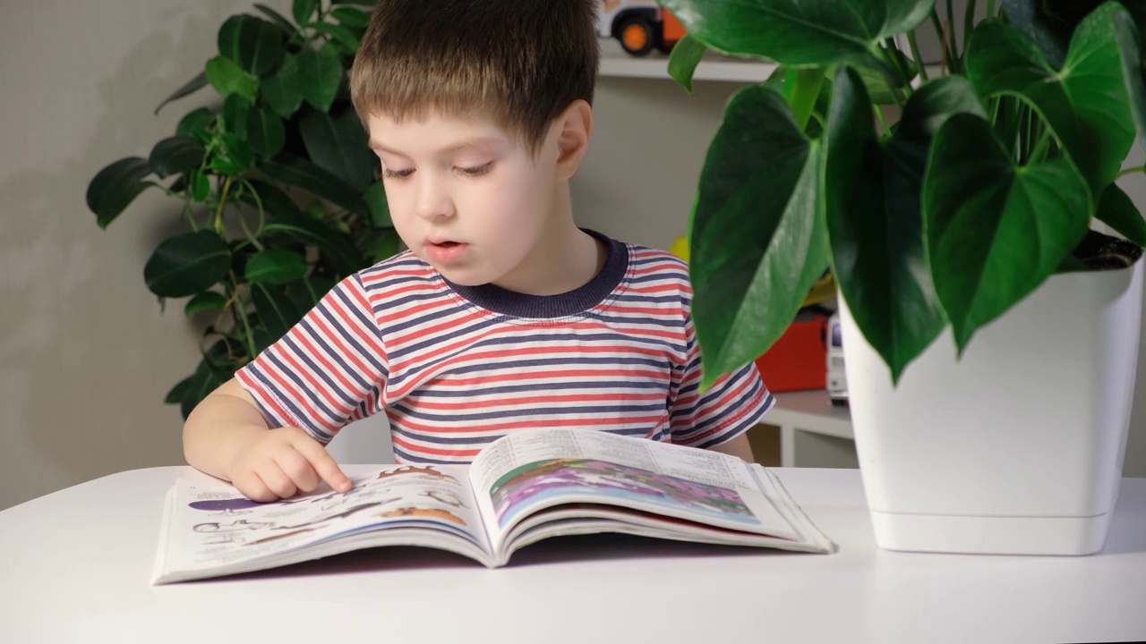 一个穿着条纹t恤的孩子学习阅读，看着图画书并说话。视频素材