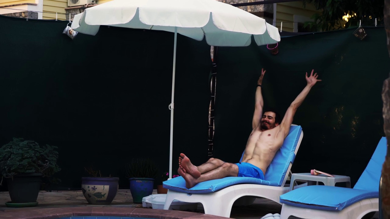 穿着泳装的男子正躺在游泳池边的躺椅上，闭着眼睛进行日光浴视频下载