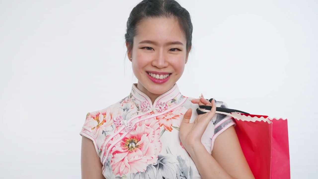 中国/亚洲妇女使用比特币购物，在中国春节期间，拿着购物袋，白色背景，穿着旗袍白色花卉图案的衣服视频下载