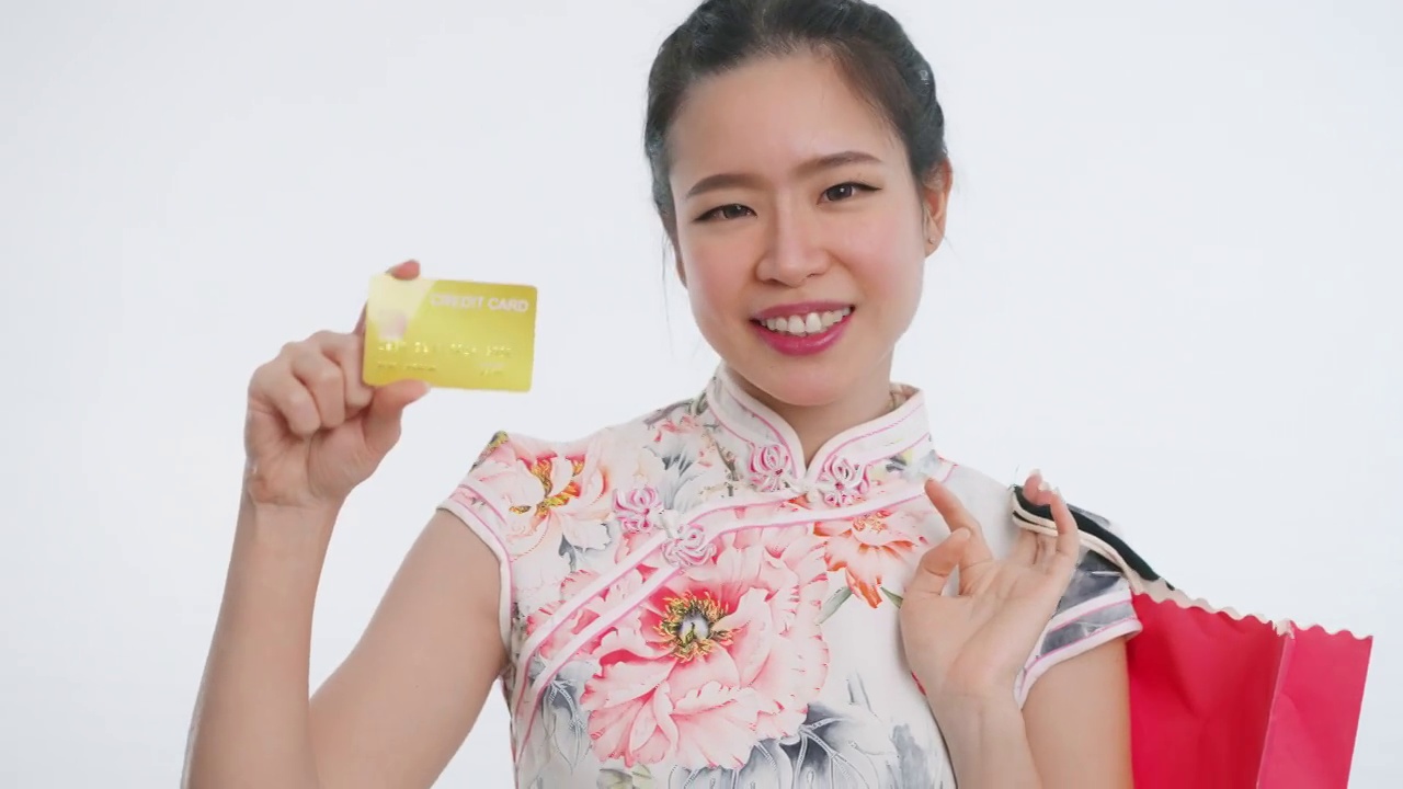 中国/亚洲妇女在春节期间用信用卡购物，手拿购物袋，白色背景，穿着旗袍白色花卉服装视频下载