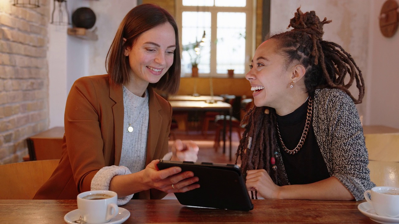 两个女商人坐在咖啡馆里，用着平板电脑视频下载