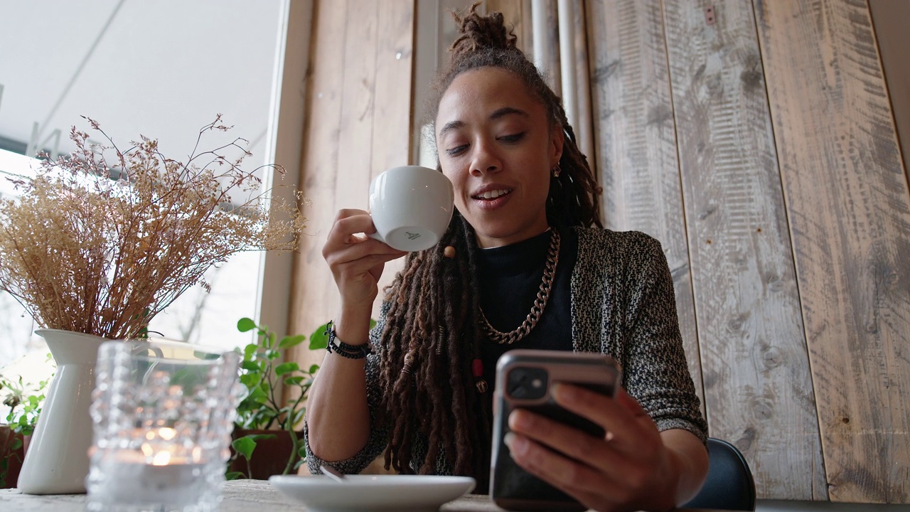 一名年轻女子在咖啡馆边喝咖啡边玩手机视频下载