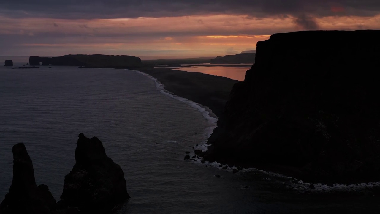 日落时的空中摇摄照片，显示玄武岩柱和Reynisfjara黑沙滩，冰岛维克视频下载