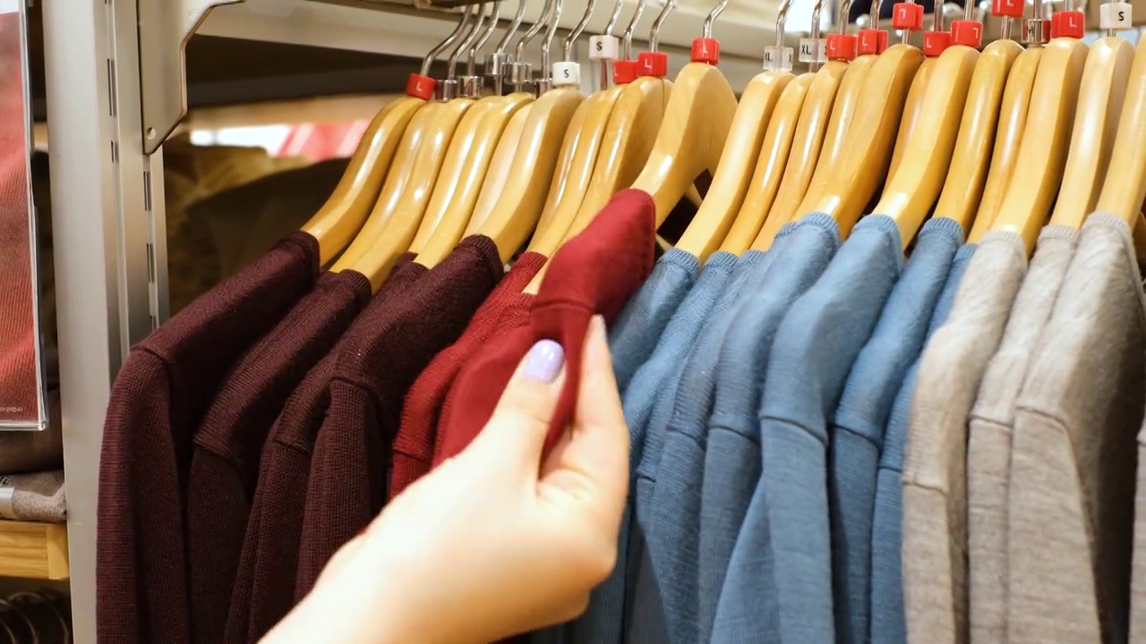 女性手在商店女装特写中挑选毛衣。视频素材