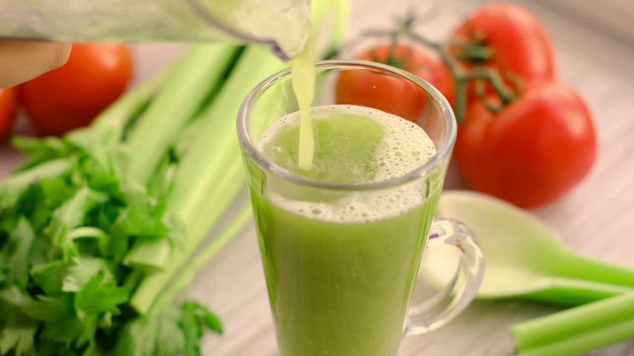 健康素食绿色芹菜奶昔。西芹汁，配上番茄小枝。芹菜汁倒进杯子里。慢动作视频下载