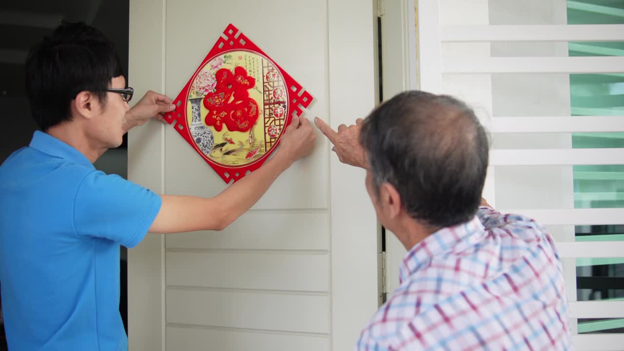 亚洲华人的儿子和父亲在中国新年前夕用“财运”春联装饰他的房子视频素材