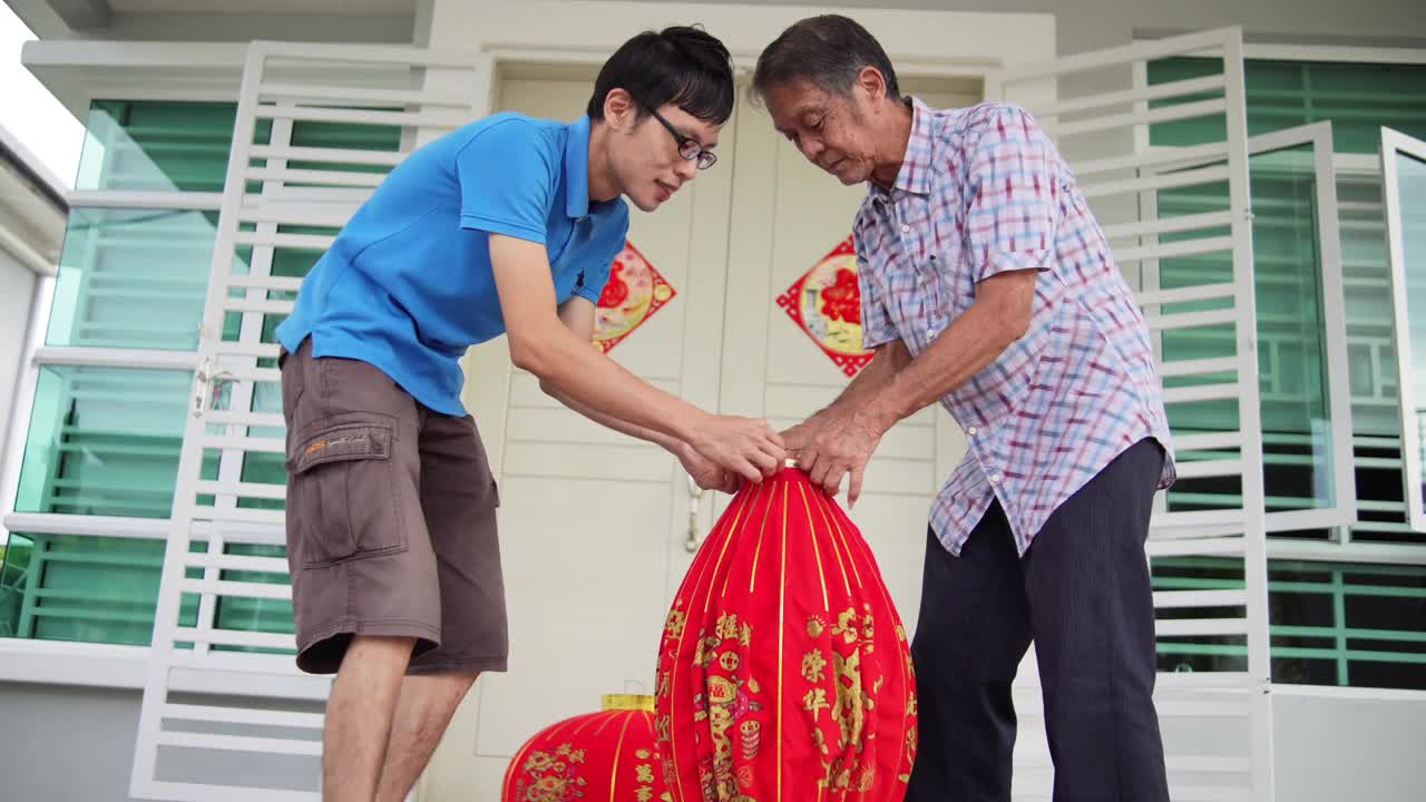 亚洲华人父亲和儿子准备大红灯笼在他们家的前院在中国新年前夕视频素材