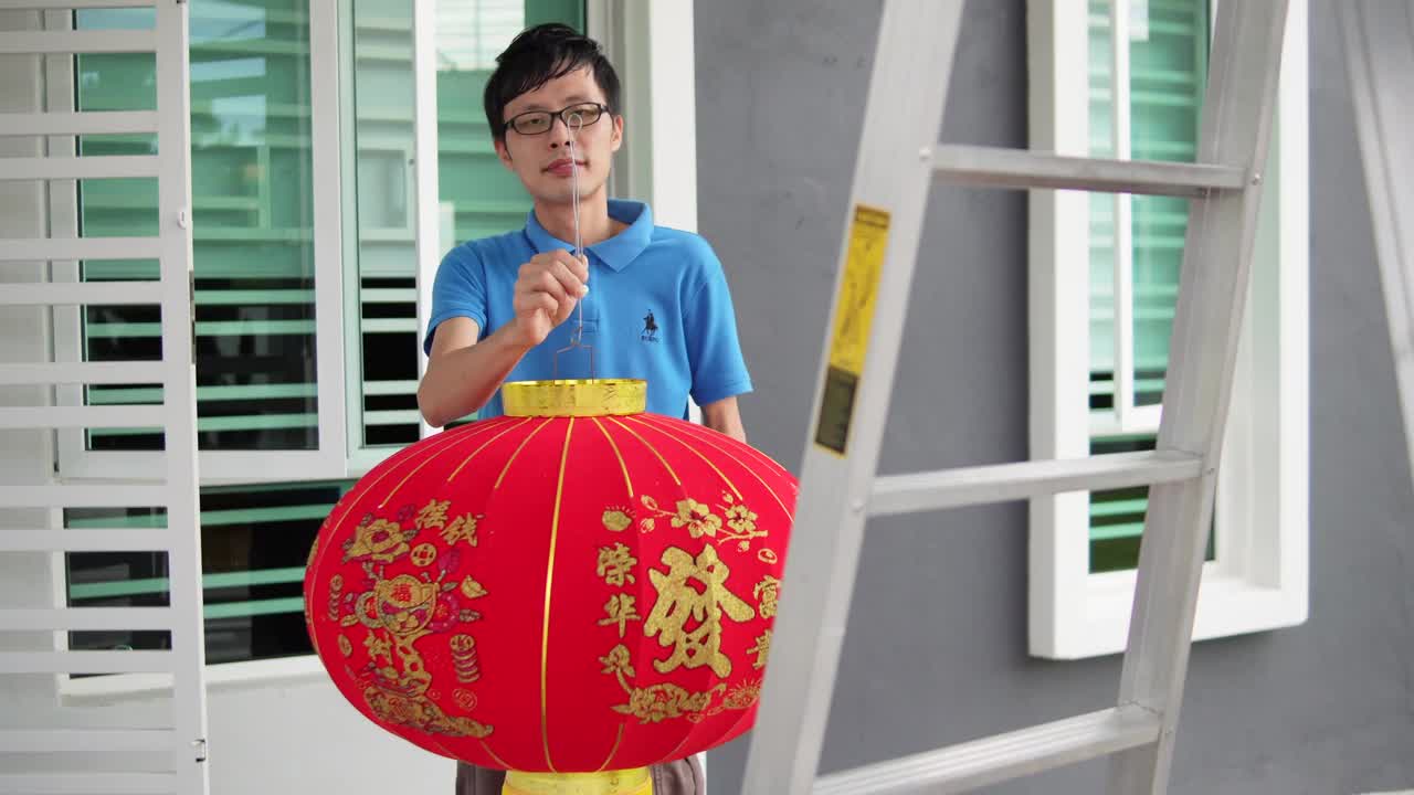 亚洲华人男子挂红灯笼在他家的前院在中国新年前夕视频素材