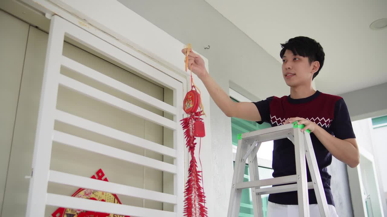 亚洲华人微笑的男性挂现代鞭炮在他的房子前在中国新年前夕视频素材