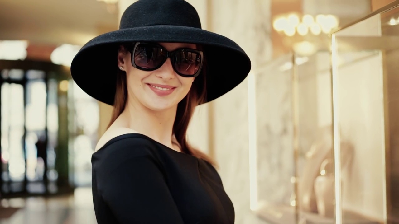 一位戴着太阳镜和帽子的穿着得体的年轻女子看着珠宝店的橱窗，让她的丈夫给她买昂贵的珠宝视频下载