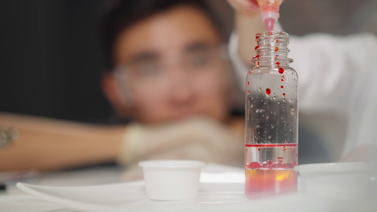 在化学测试中，女孩将红色颜料滴入透明液体中视频下载