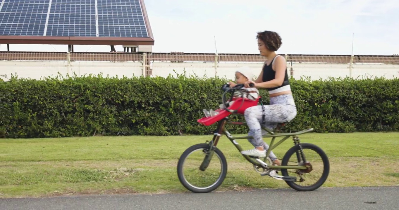 一辆母亲的自行车和一辆父亲带着两岁男孩的自行车一起行驶在太阳能电池板前面的道路上。视频下载