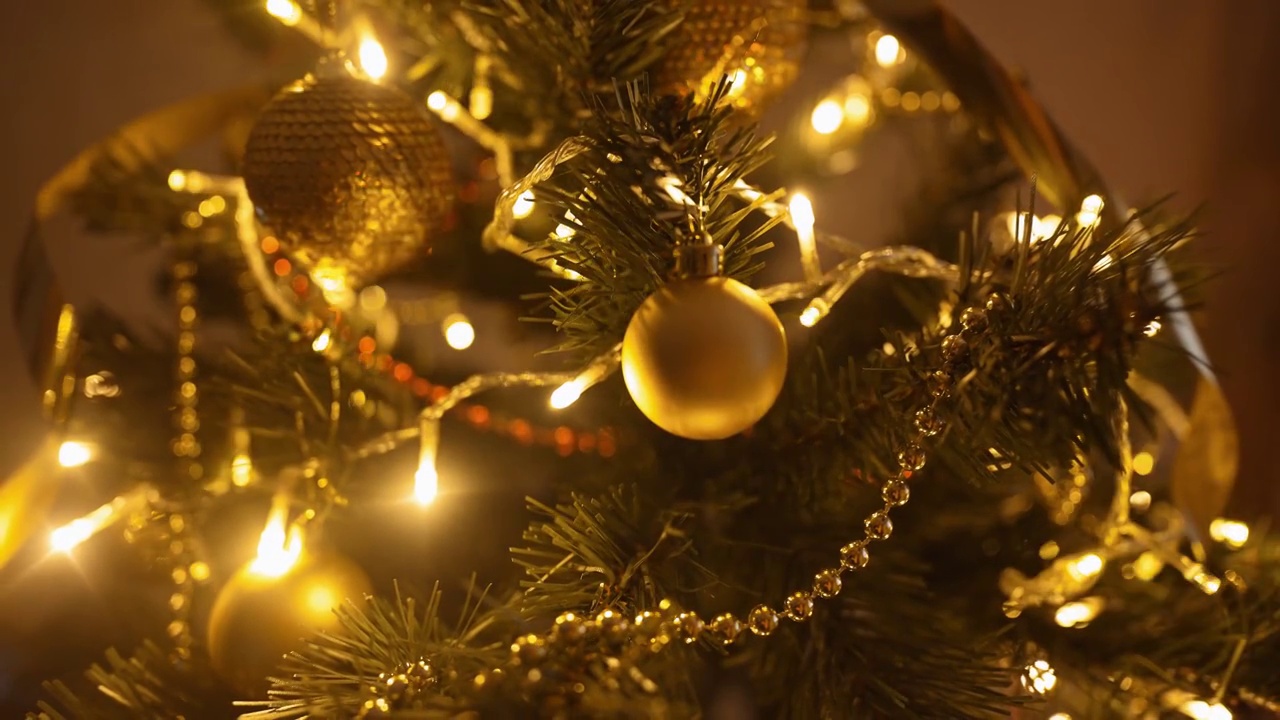 慢动作特写挂在室内圣诞树树枝上的金色装饰球。装饰房子，准备在家里庆祝圣诞节和新年视频素材