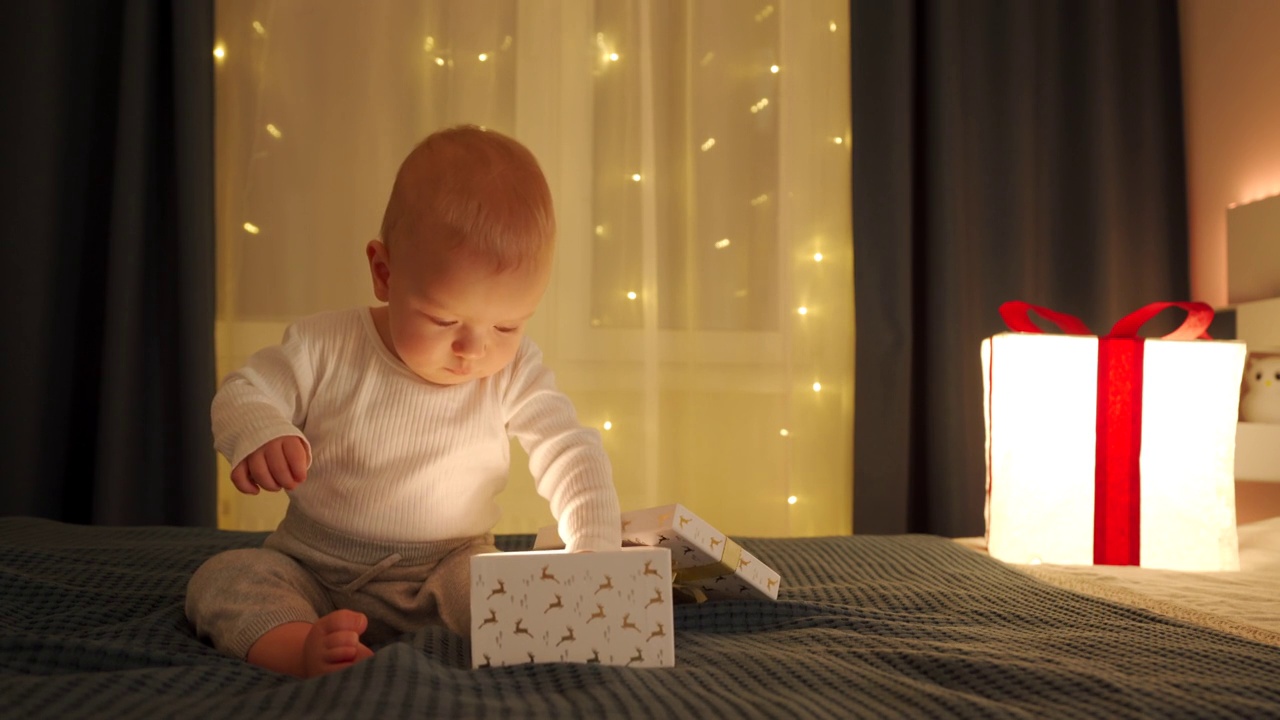 可爱的小男孩拿着圣诞或生日礼物，白种人小孩在卧室的床上打开礼盒。生日、圣诞节、新年庆祝理念。视频下载