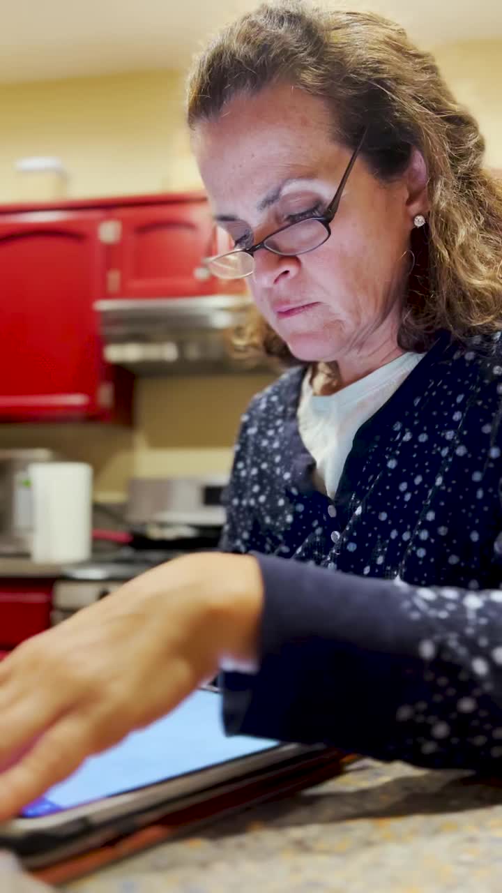 成熟的女人坐在厨房里用她的数码平板电脑视频素材