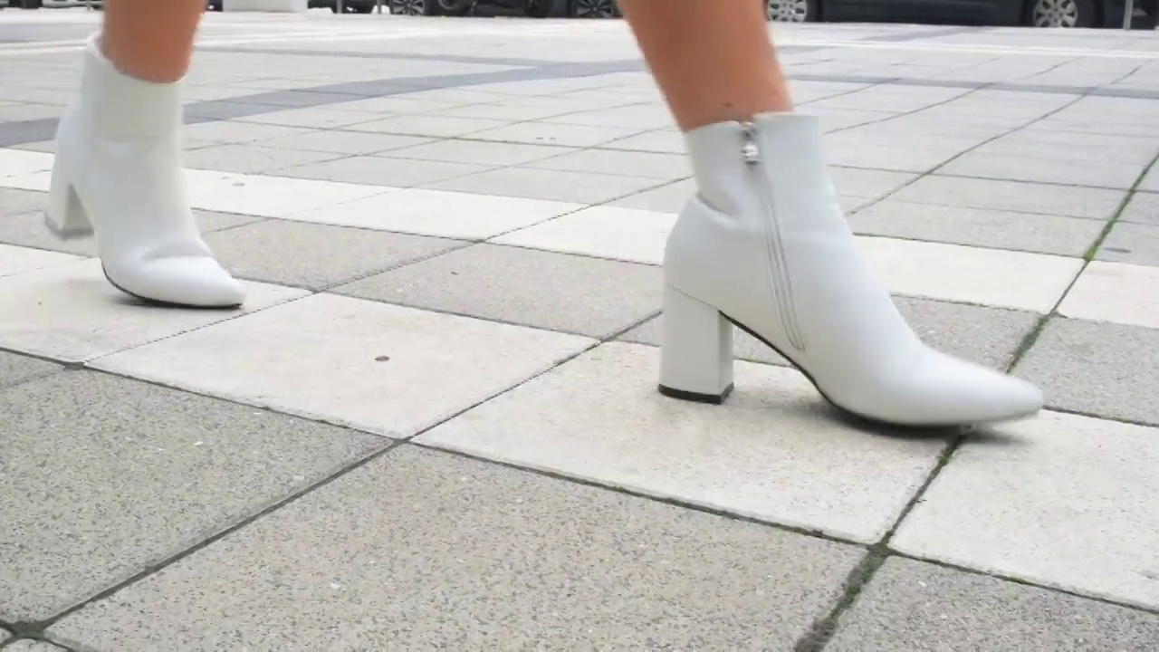 模特的双腿穿着黑白相间的鞋子，走在铺着瓷砖的城市道路上。视频素材