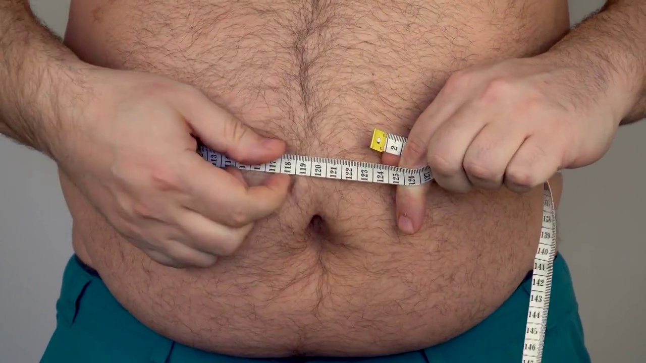 一个胖子用厘米的卷尺测量腹部的大小。这个人体重超标。大肚子多毛的男人视频素材