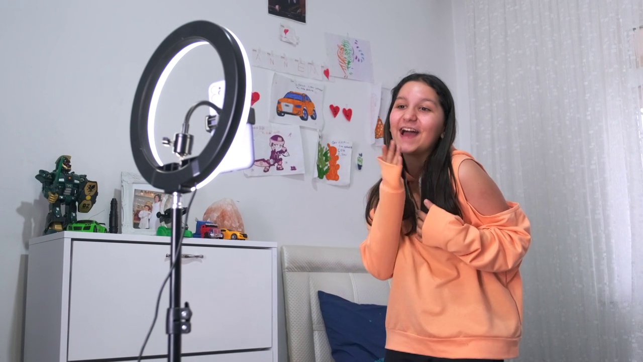 侧视图画像的十几岁的女孩在家里拍摄视频和跳舞的相机设置在环灯，年轻的博主概念，复制空间视频下载
