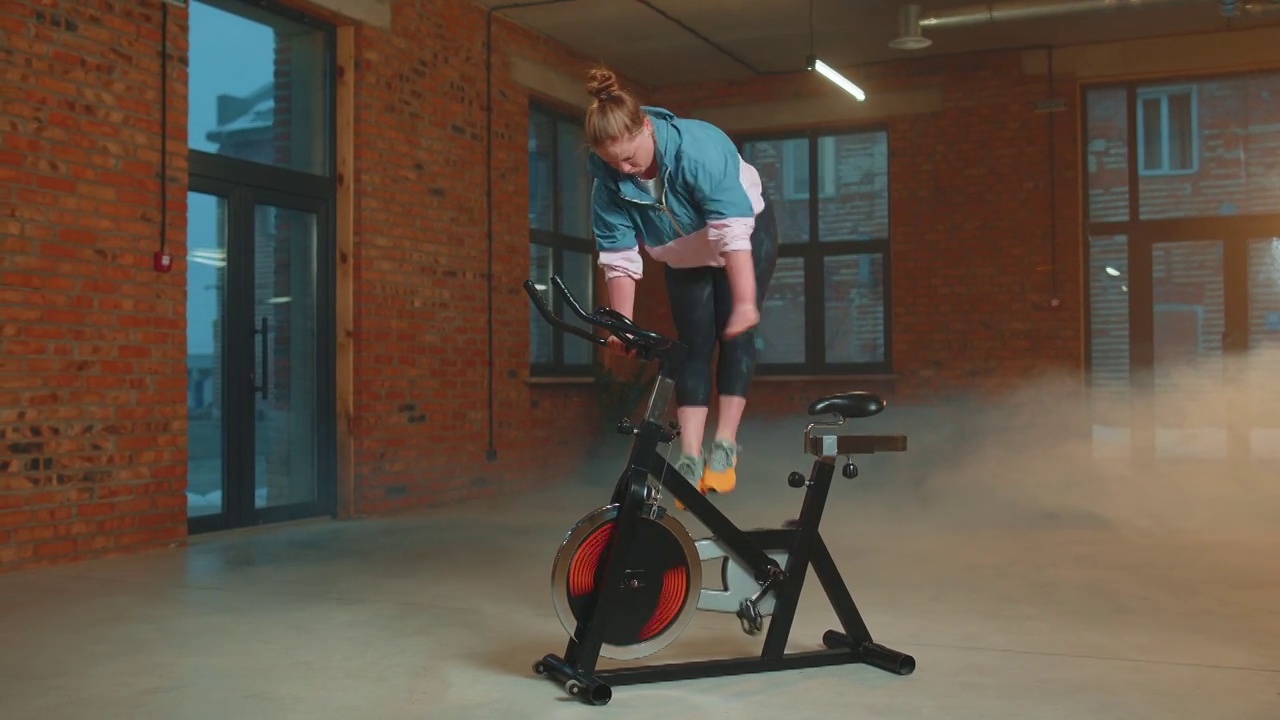 女运动员骑动感单车在雾霾体育馆进行常规训练，在室内减肥视频下载