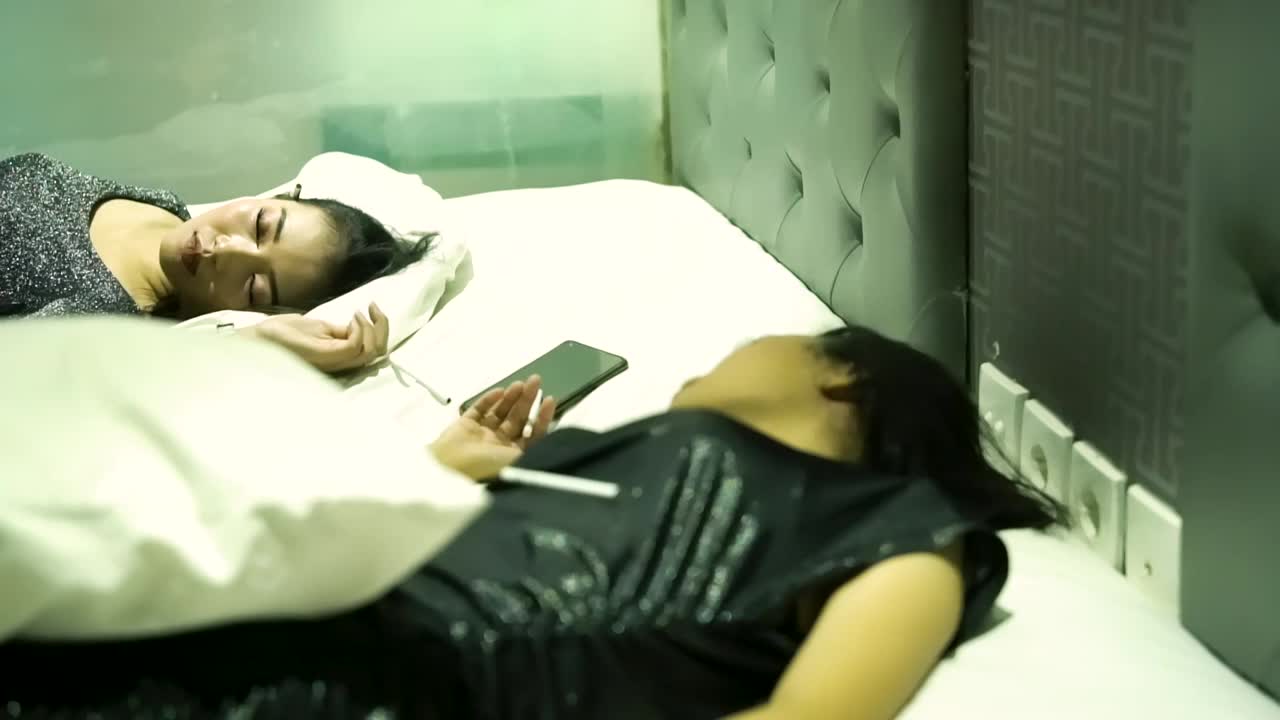 两个性感的女人在喝酒抽烟后睡在白色的床上视频下载