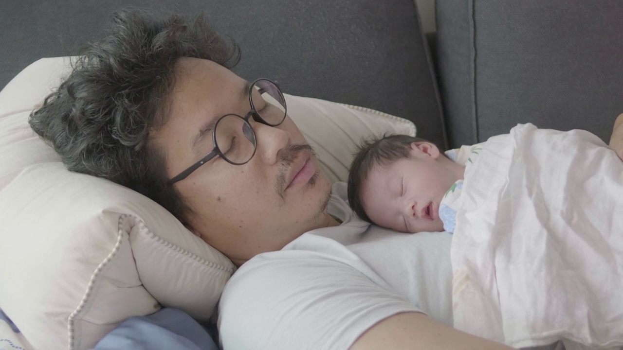 4k幸福疲惫的亚洲父亲和儿子睡在沙发上早上。视频下载