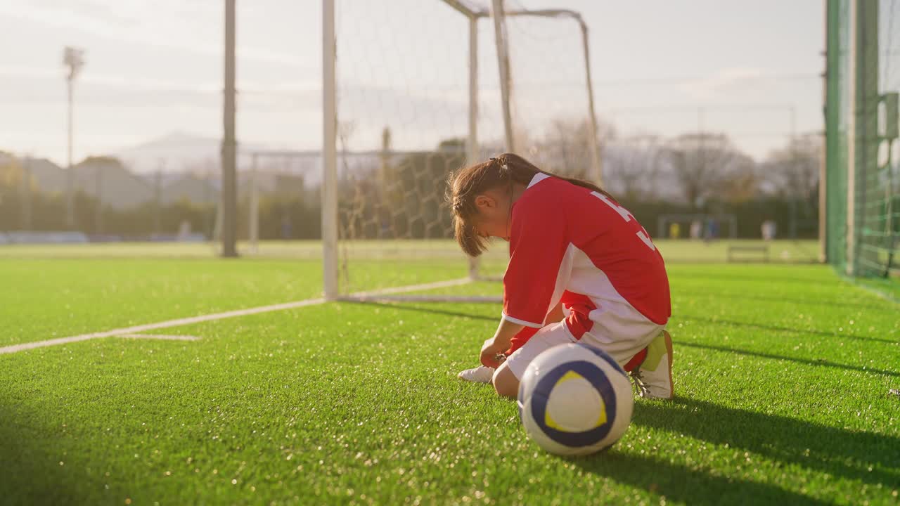 女小学足球运动员系上足球或足球鞋，然后拿着足球走进足球场视频下载