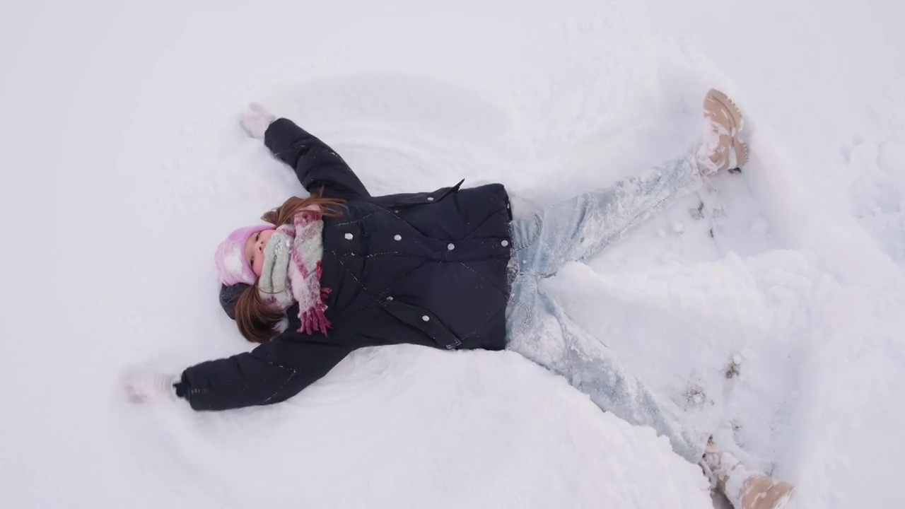 快乐的小女孩躺在雪地里，做了一个雪天使。圣诞节假期,假期视频素材
