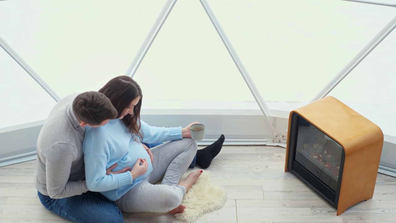 一对即将生孩子的年轻夫妇在壁炉边喝热饮视频下载