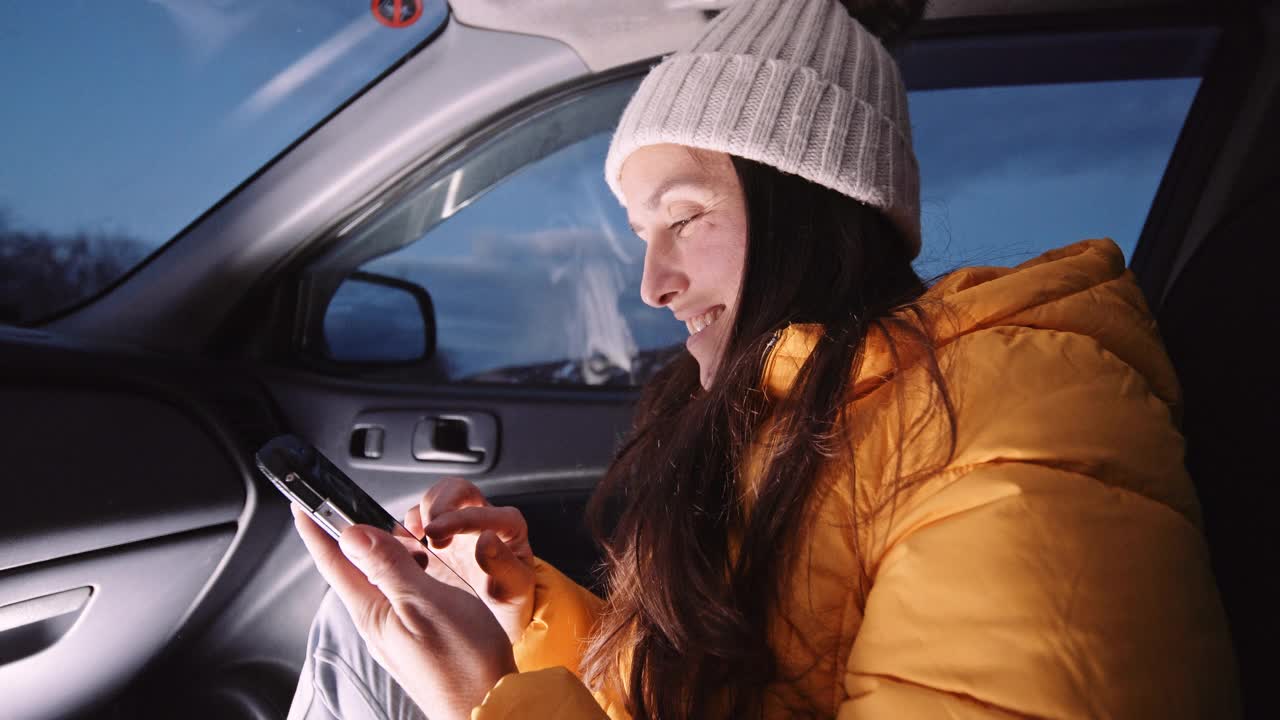 微笑的女人在车里用手机浏览婴儿照片。视频下载