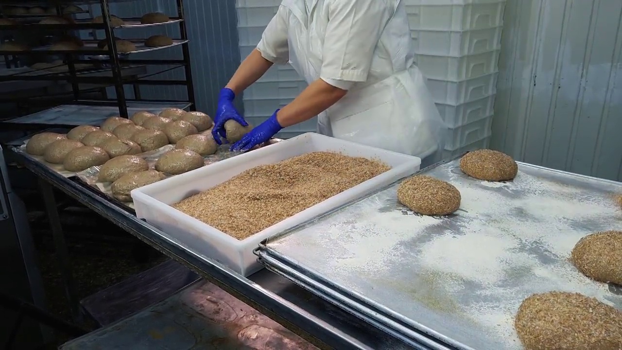 女工人在烤面包前用面包屑把新鲜的面包卷起来。视频下载