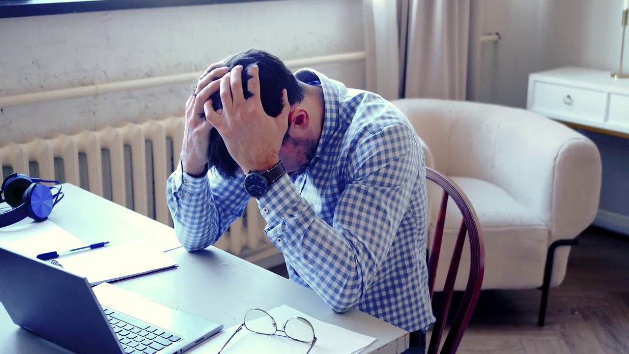 疲惫的男人在笔记本电脑前在家里-自由职业者过度工作的家庭概念视频下载
