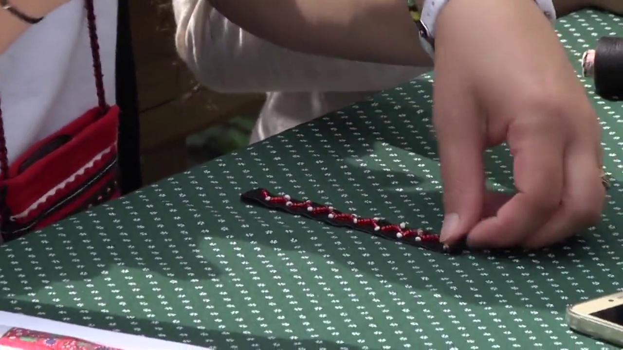 在房子的院子里，一个女人的手在桌子上缝着一条带红珠子的丝带65a视频下载