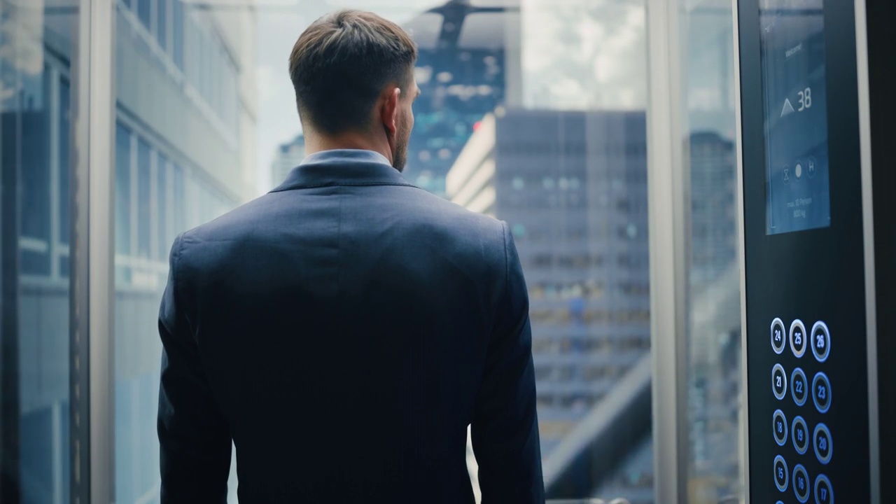 西装革履的成功商人乘坐玻璃电梯到现代商务中心办公。一名年轻男子从电梯的全景窗口看现代市中心摩天大楼。视频下载
