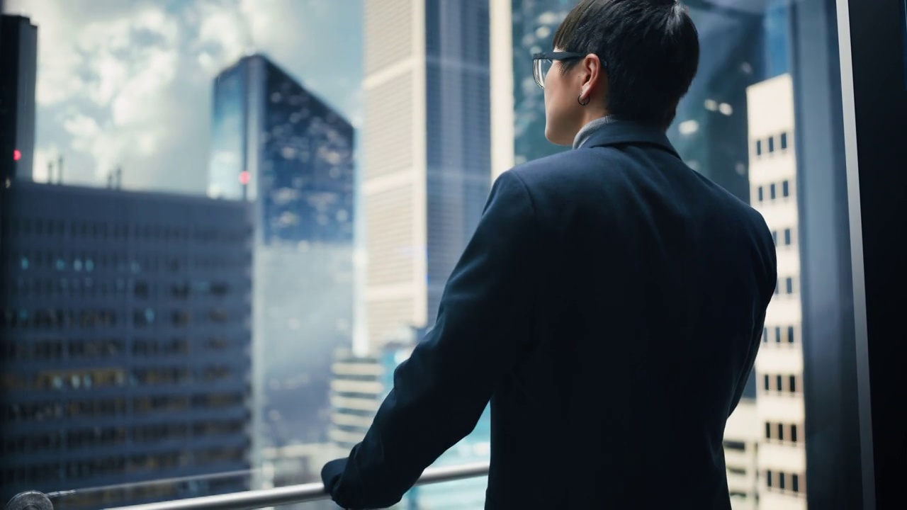 时尚的日本商人乘坐玻璃电梯到现代商务中心的办公室。从电梯的全景窗口看现代市中心的摩天大楼。转身对着镜头。视频素材
