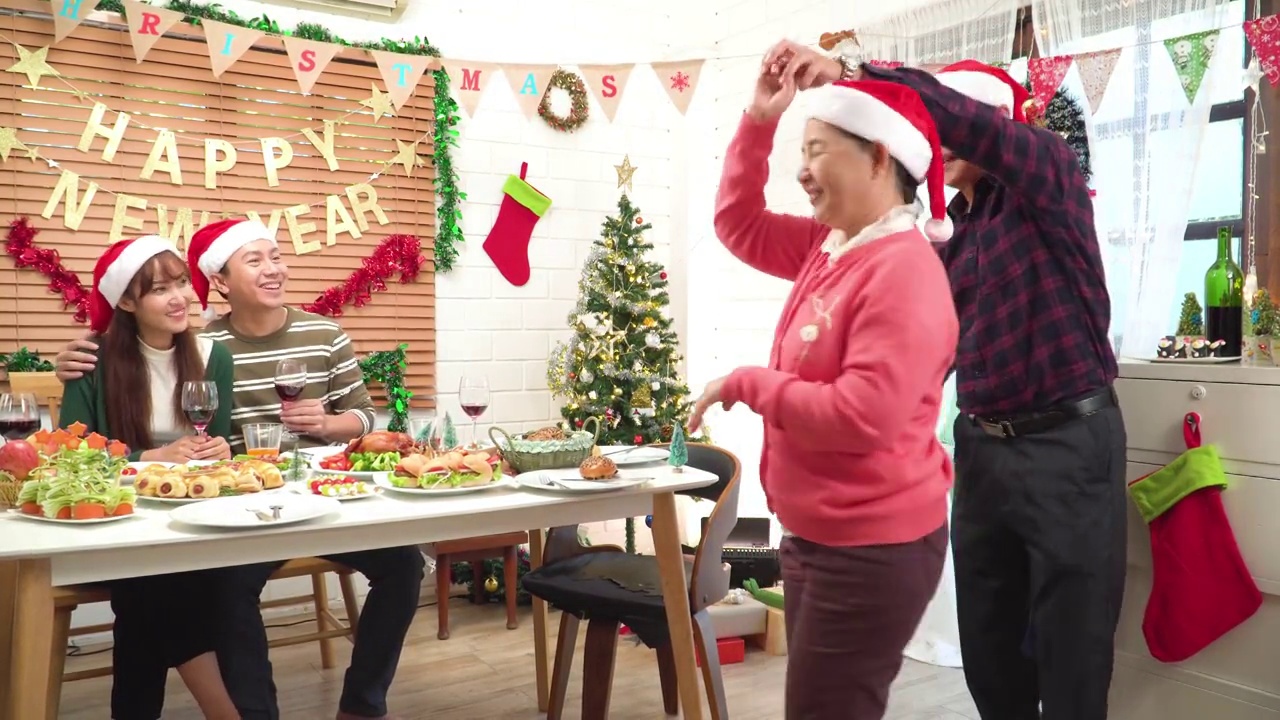 亚裔父母开心地跳舞，成年女儿和女婿坐着，唱着歌，欢呼着，在装饰好的餐厅里一起度过12月的美好时光视频下载