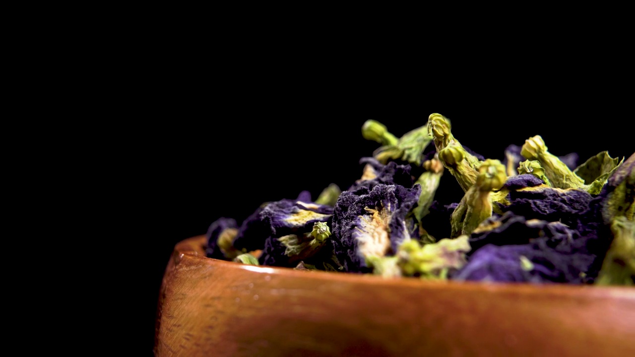 常熟干蝶花。蓝色干燥阴蒂在黑色背景的木碗。宏视频下载