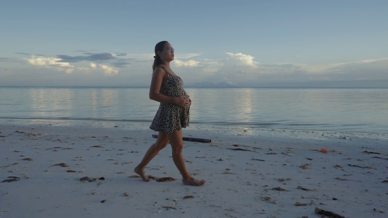 怀孕的亚洲妇女走在海滩上日落视频下载