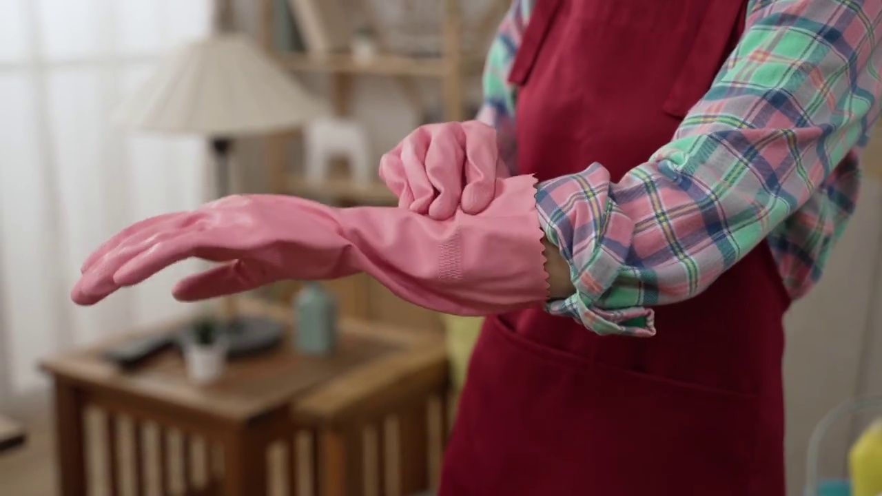 女人在做家务前戴着橡胶防护手套的特写。在准备打扫房间时，专注于女佣的手穿上粉红色的手保护。家务的概念视频素材