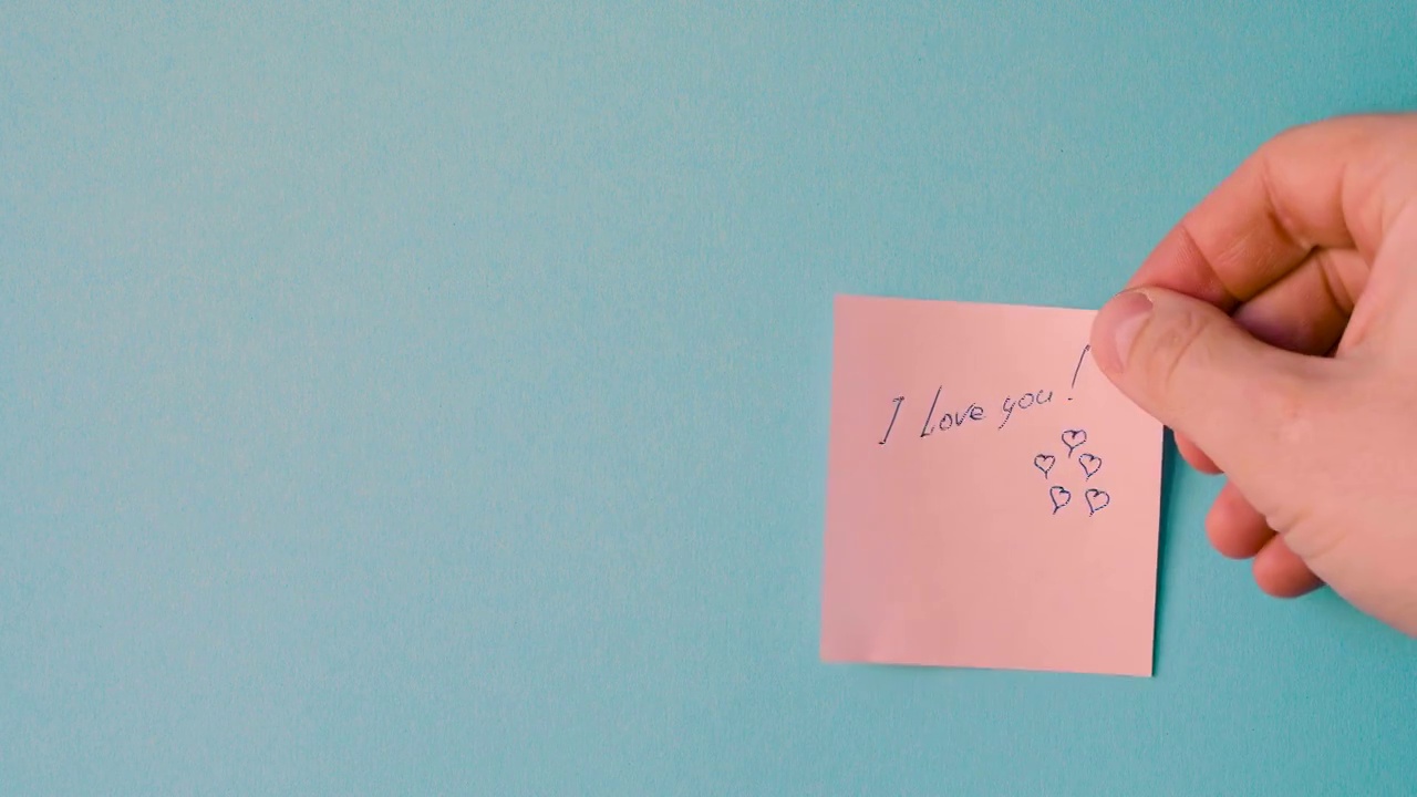 一名男子的手正在用蓝色的底色，用钢笔写下“我爱你”和“情人节的爱心”视频下载