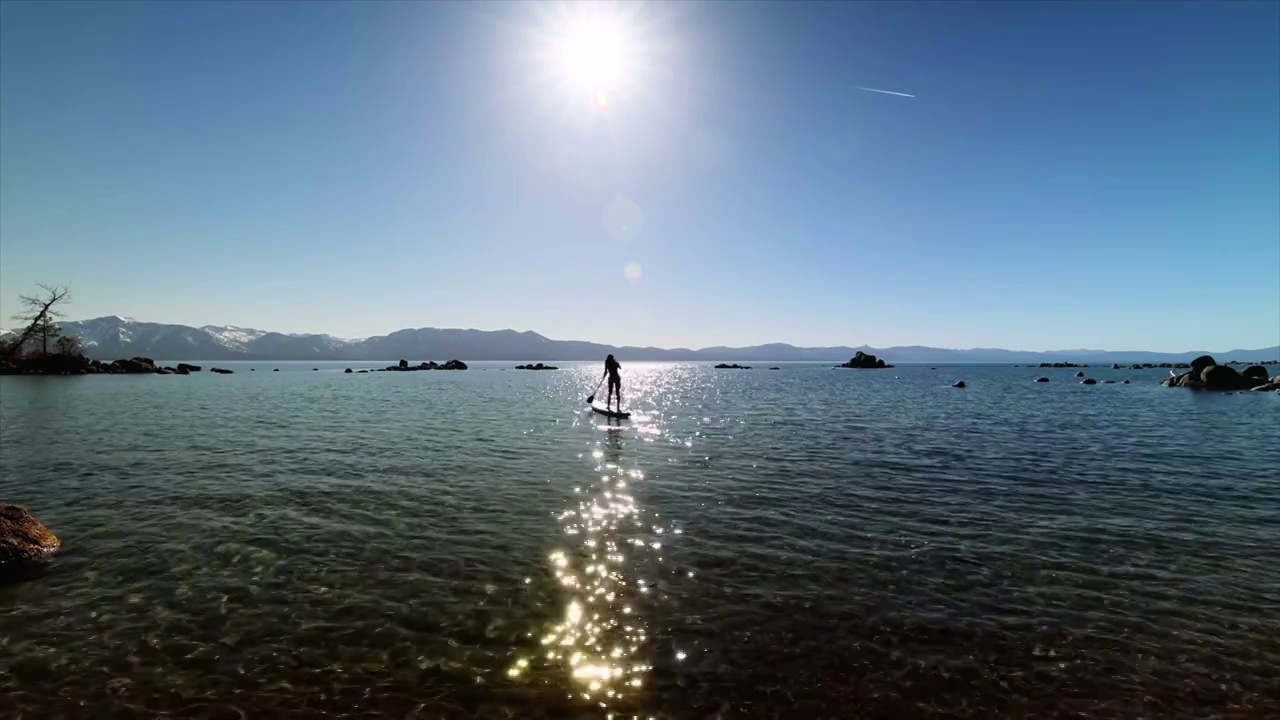 女人站在划桨冲浪在平静的湖在山顶下太阳视频素材